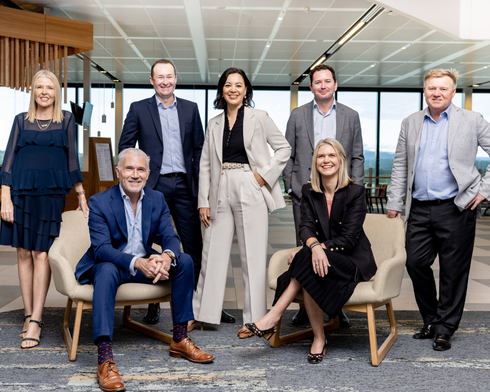 A group of executives indoors with seated and standing members in business attire.