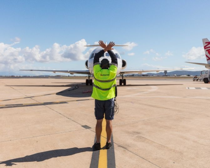 Townsville airport ground crew member signaling aircraft to stop with crossed arms, demonstrating standard safety protocol.