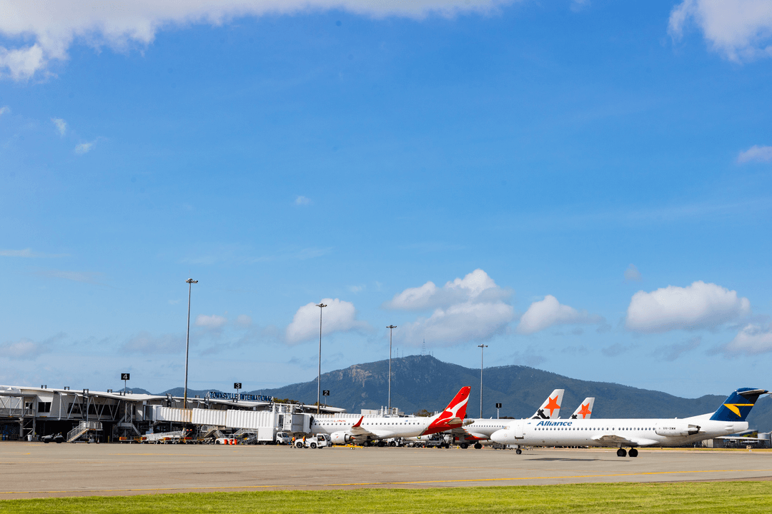 Townsville Airport tarmac with Qantas and Alliance aircraft at gates, terminal and mountains in background.