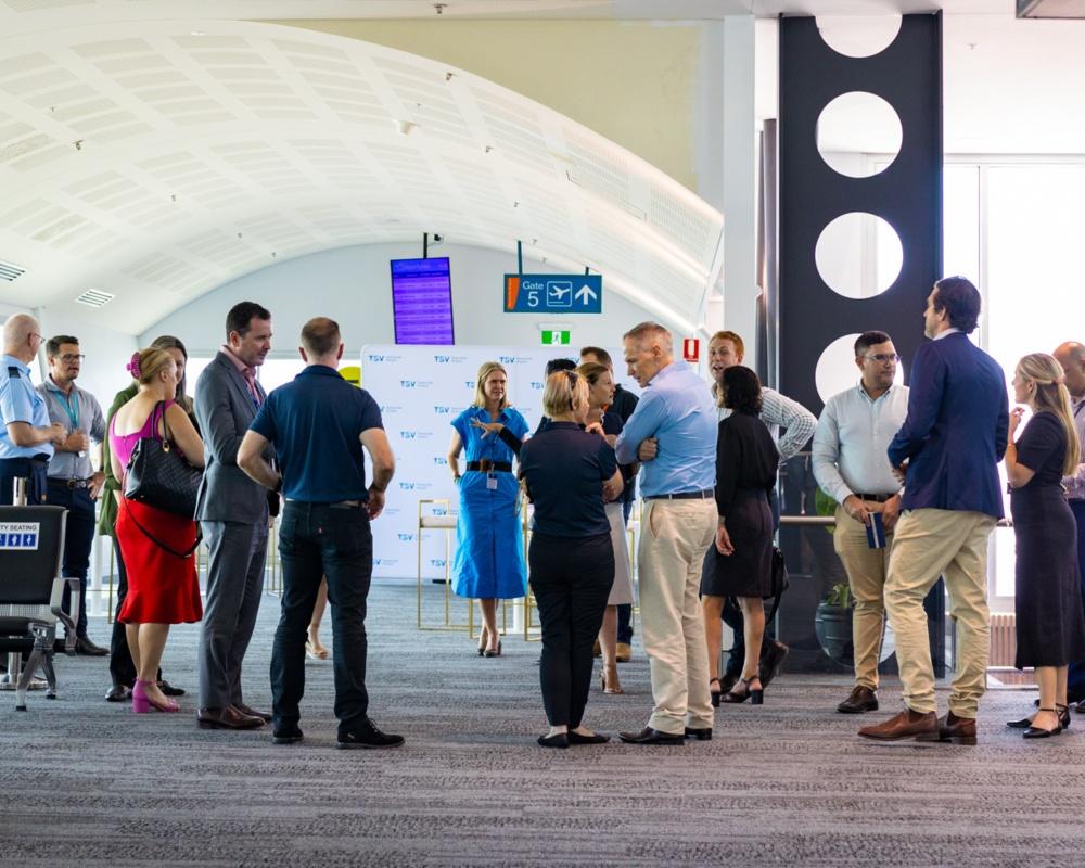 Community consultation group meeting inside Townsville Airport terminal, with participants conversing beneath curved ceiling panels and directional signage.