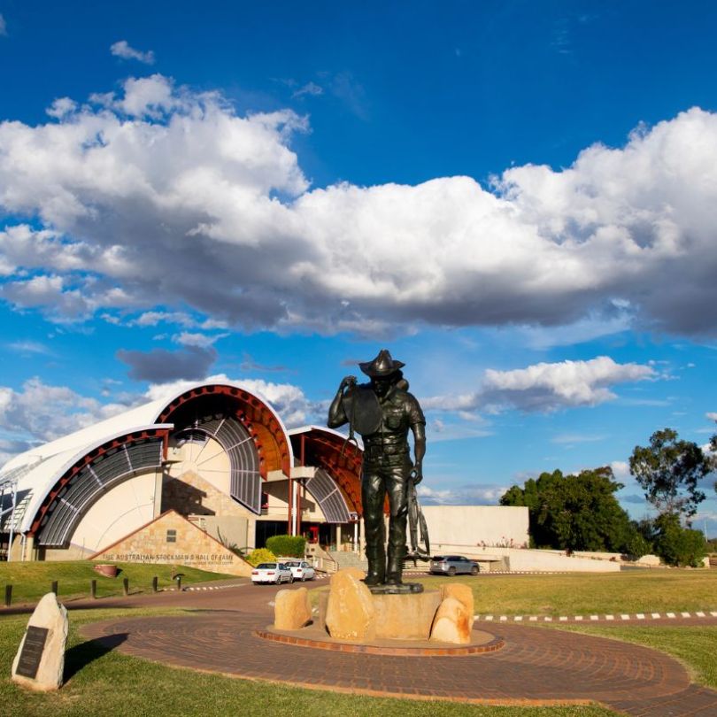Bronze statue of a stockman in front of the Australian Stockman’s Hall of Fame under a blue sky with scattered clouds, Longreach.