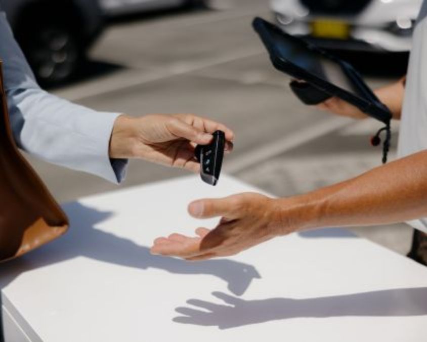 Close-up of a car key being handed over between two people at a white counter in an outdoor area near Gold Coast Airport.