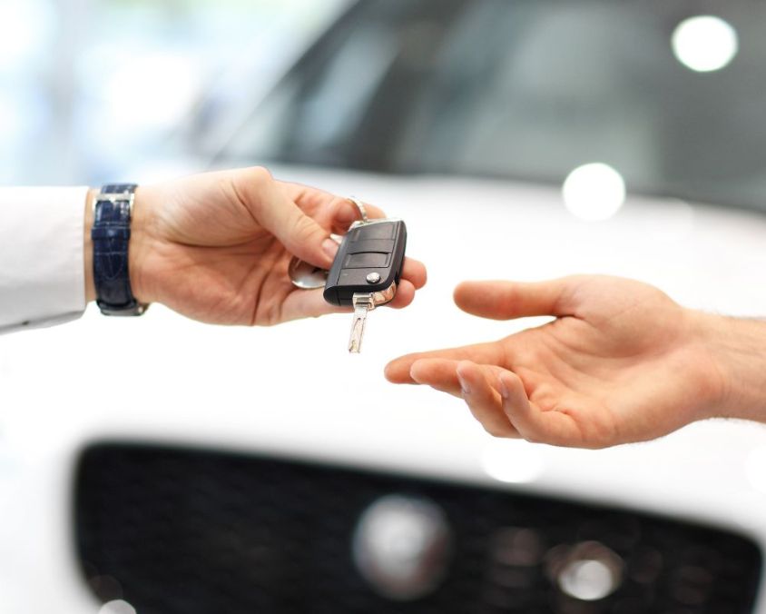Close-up of hands exchanging car key in front of a white vehicle.