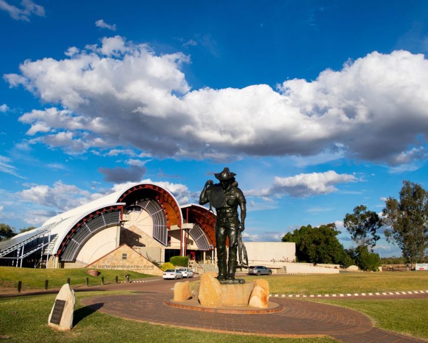 Bronze statue of a stockman in front of the Australian Stockman’s Hall of Fame under a blue sky with scattered clouds, Longreach.