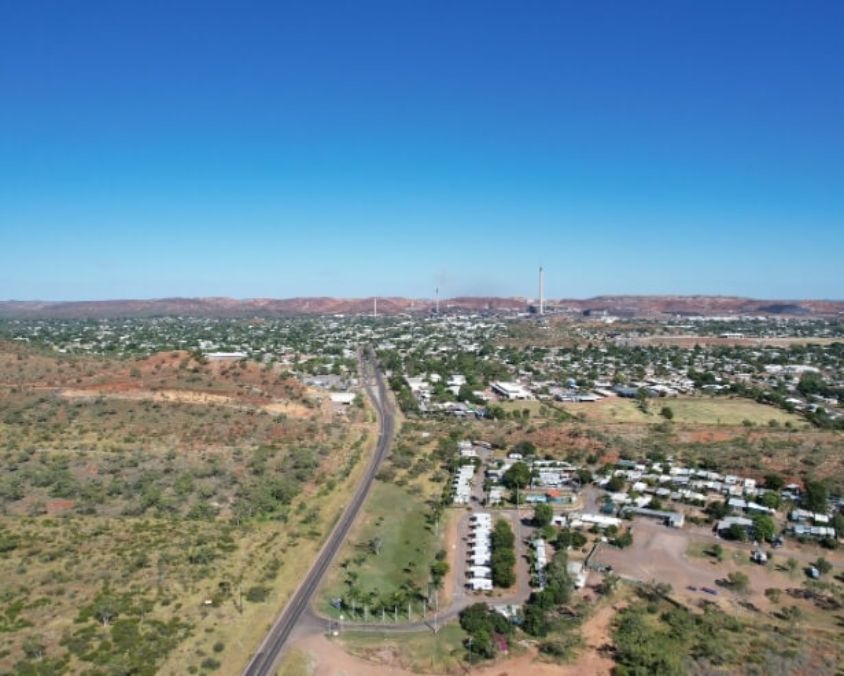 An Aerial view of Mount Isa town surrounded by semi-arid landscape, with a main road leading through sparse vegetation toward buildings and industrial facilities.