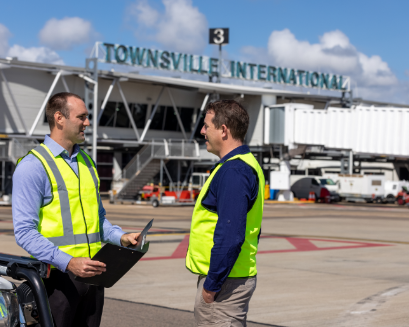Airside view at Townsville Airport with staff in high-vis vests near terminal and gate 3 signage.