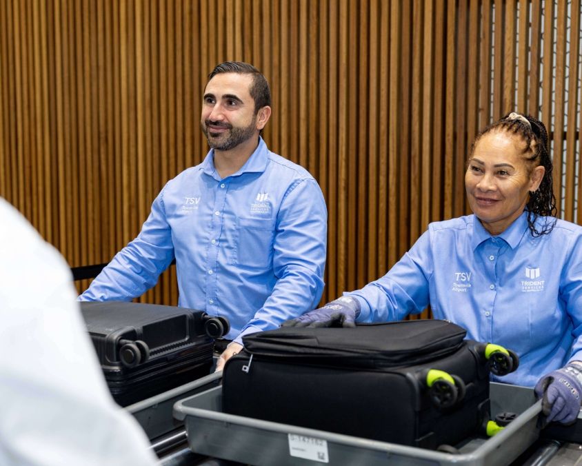 Two uniformed staff members at a Townsville Airport luggage screening counter, handle baggage trays. 