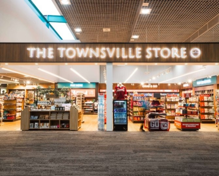 Entrance to The Townsville Store’ featuring illuminated signage and a well-organised interior with books, snacks, beverages, and sports apparel on display. 