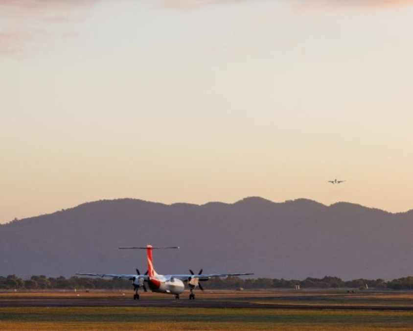Two aircraft at Townsville Airport, one on the runway and another airborne, set against a backdrop of hills and a clear sky. 