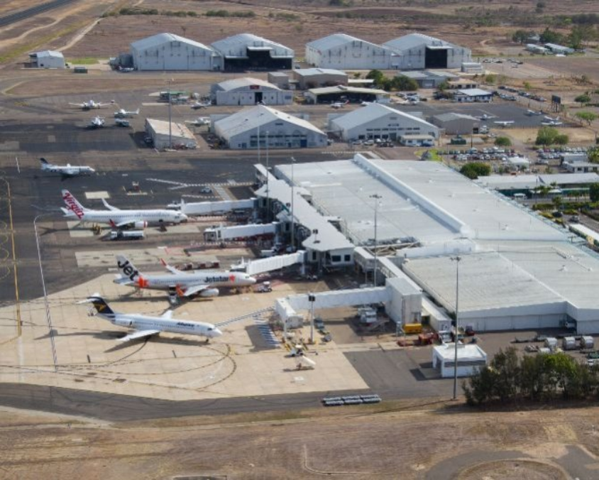 Aerial view of the Townsville airport terminal with multiple airplanes from various airlines, including Virgin Australia and Jetstar, parked at gates and connected by jet bridges.